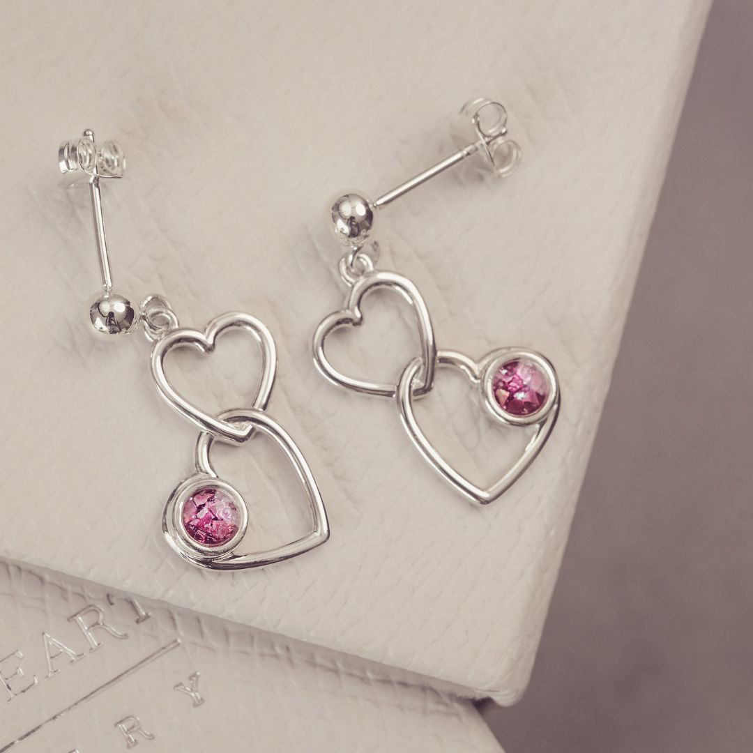 two silver heart earrings with pink gemstones on a grey background