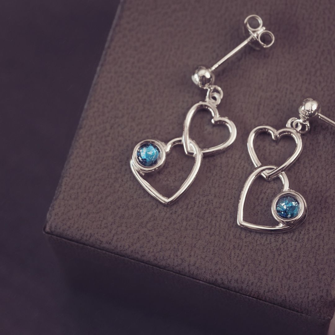 two silver heart dangle earrings with blue genstones on a dark purple background