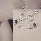 two silver heart dangle earrings with black gemstones on a silver and grey background
