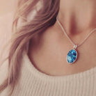 A lady's neckline showing a silver and blue oval cremation ashes necklace. 