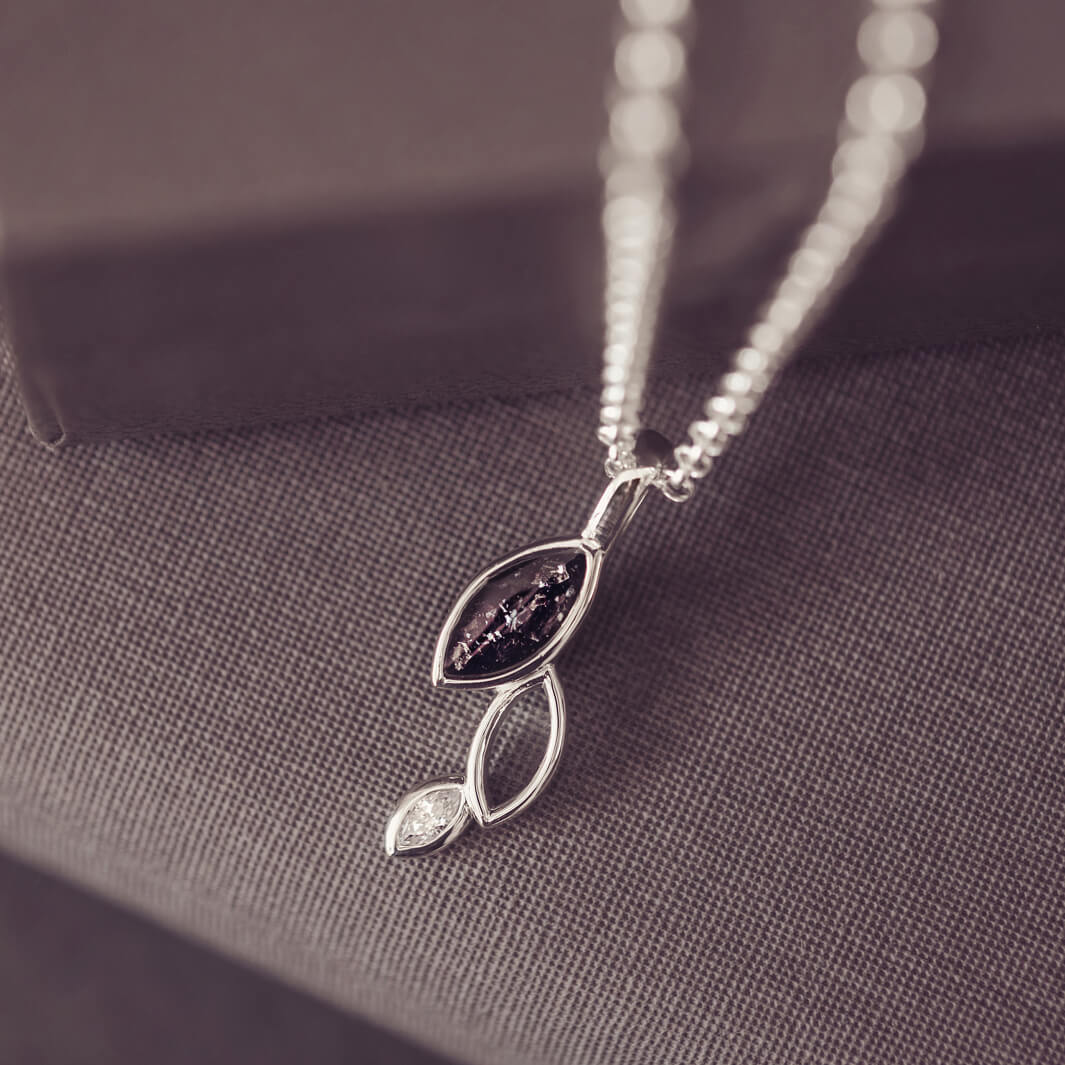 sterling silver necklace featuring gem stone, cremation ashes, black crystal and resin hung over a grey box