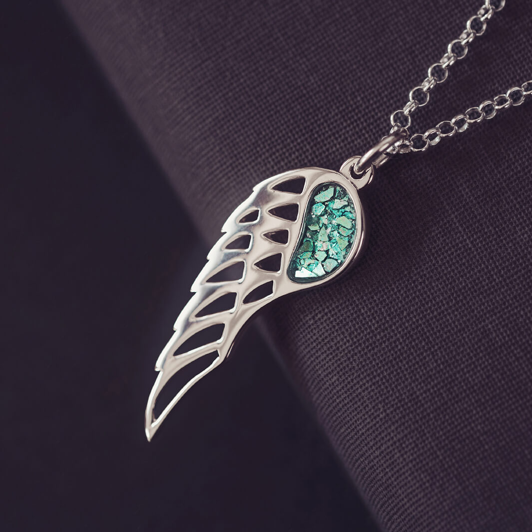 Silver Angel Wing Necklace with green floating crystals which hold cremation ashes. Shown on a dark background