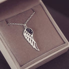 Silver Angel Wing Necklace with black floating crystals which hold cremation ashes. Shown on in a grey jewellery box 