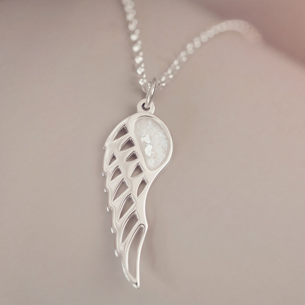 Silver Angel Wing Necklace with clear floating crystals which hold cremation ashes. Shown on a light grey background 