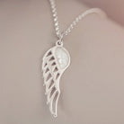 Silver Angel Wing Necklace with clear floating crystals which hold cremation ashes. Shown on a light grey background 