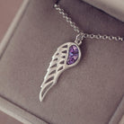 Silver Angel Wing Necklace with purple floating crystals which hold cremation ashes. Shown in a grey jewellery box 