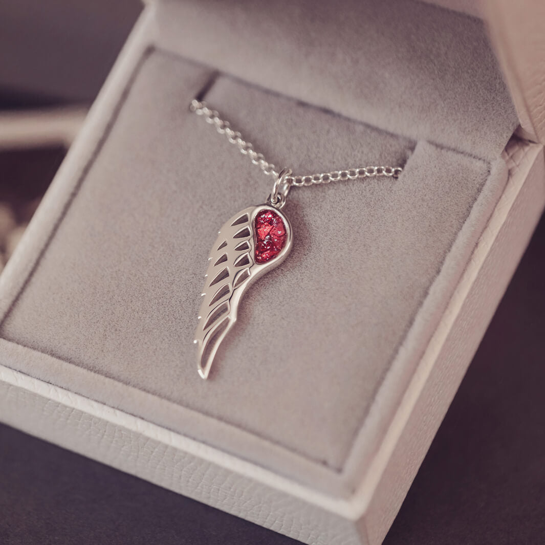 Silver Angel Wing Necklace with red floating crystals, which holds cremation ashes. Shown in a grey jewellery box 