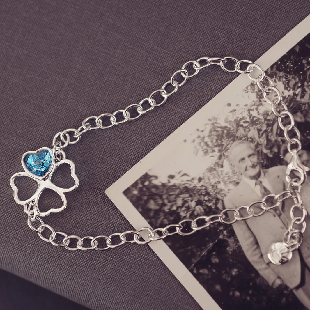 sterling silver chain bracelet with clover shaped charm holding blue crystal and cremation ashes sat on top of a black and white photo 