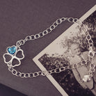 sterling silver chain bracelet with clover shaped charm holding blue crystal and cremation ashes sat on top of a black and white photo 