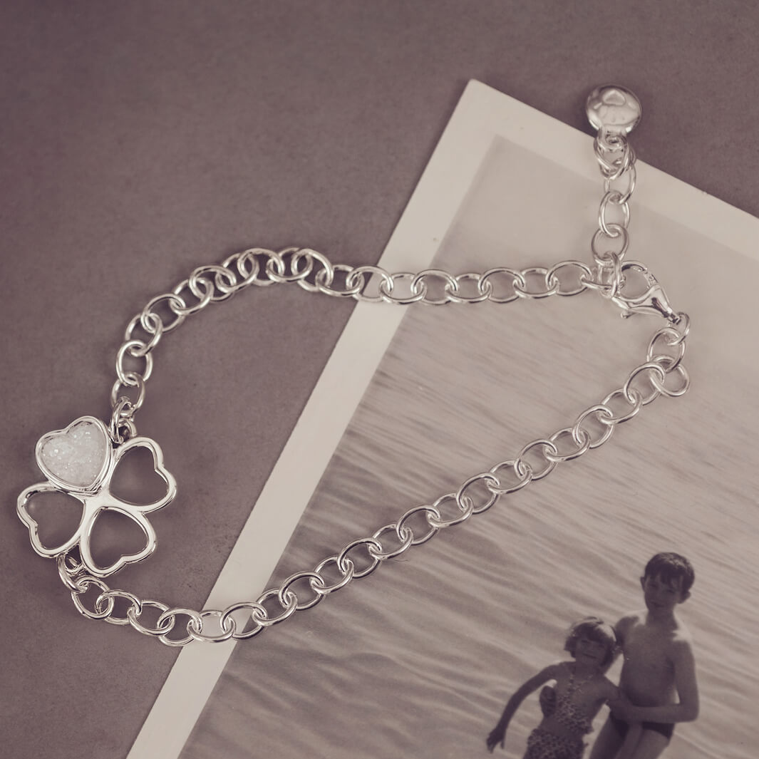 sterling silver chain bracelet with clover shaped charm holding clear crystal and cremation ashes sat on top of a black and white photo 