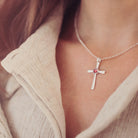 silver cross necklace with a section of resin and red crystals, holding memorial ashes, worn around a ladies neck