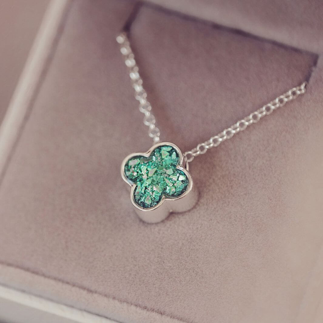 Silver necklace with a green clover-shaped pendant on a soft pink background