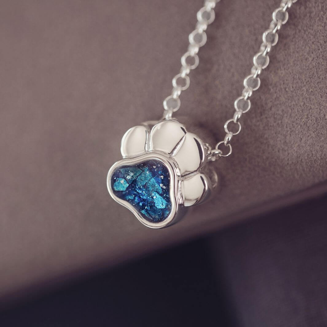 Silver necklace with a paw-shaped pendant featuring a blue gemstone on a brown background