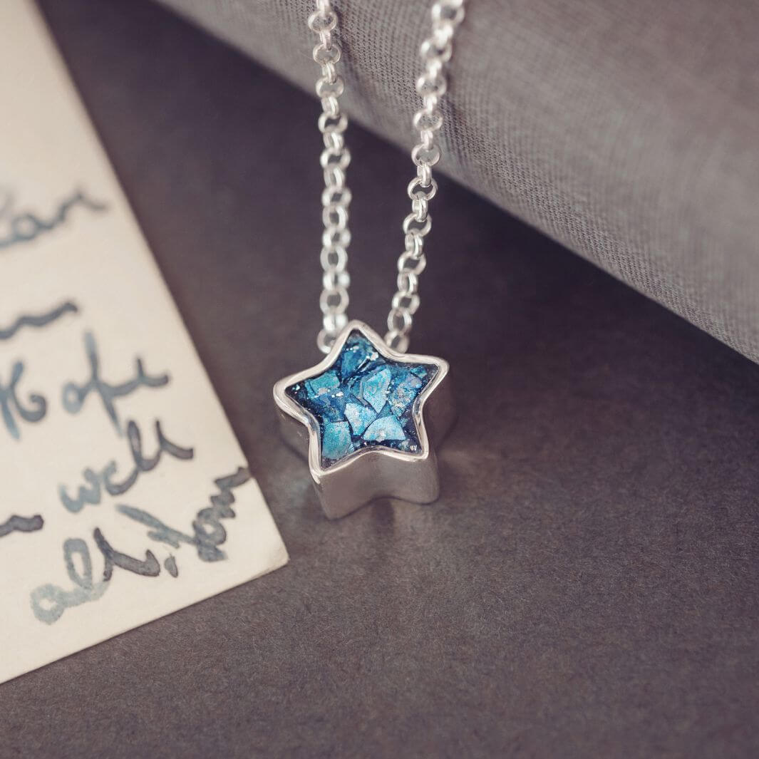 Star-shaped pendant with blue resin gemstone on a silver chain, placed on a textured surface.