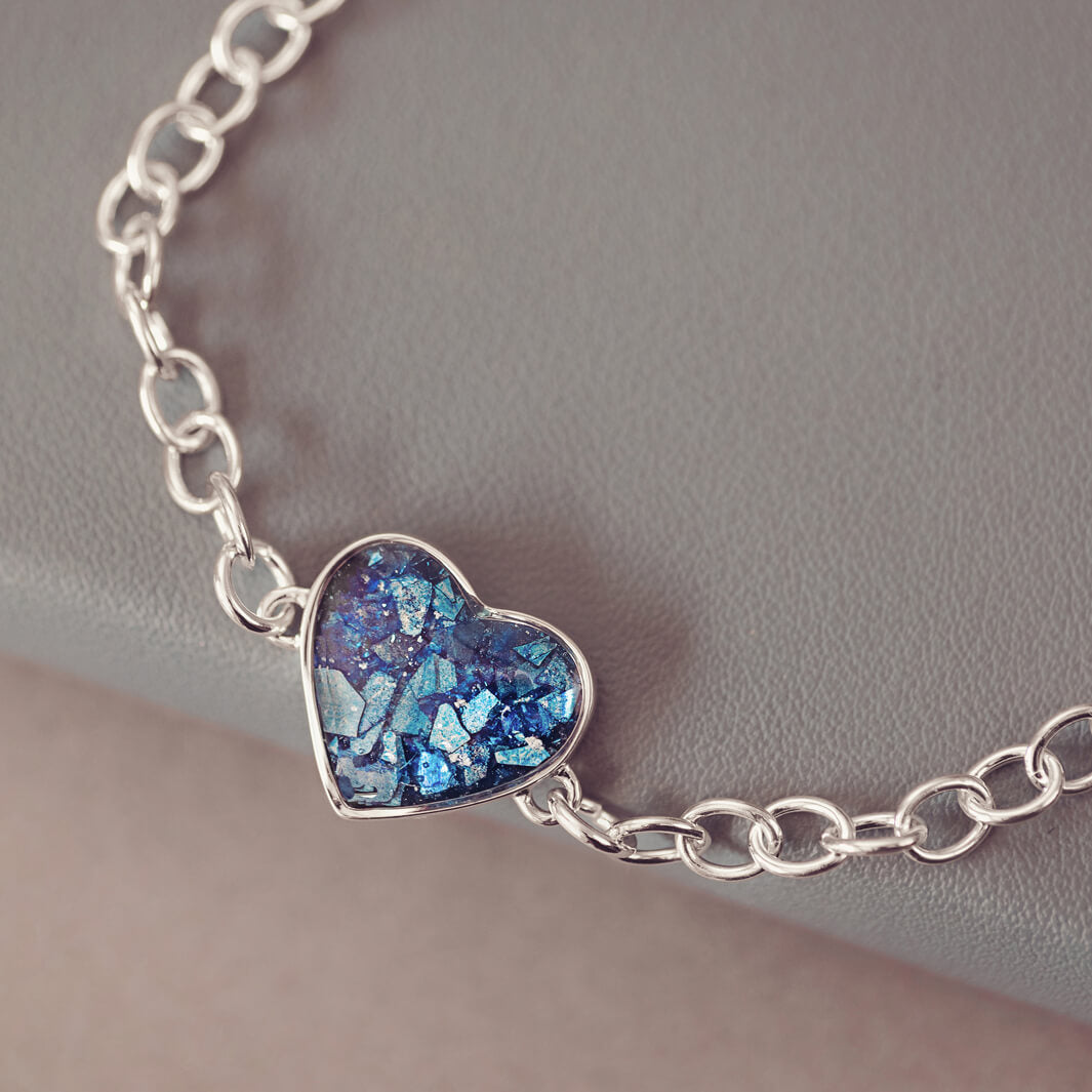 silver bracelet & heart charm, holding blue crystal, resin & cremation ashes. laying on a black grey ground 