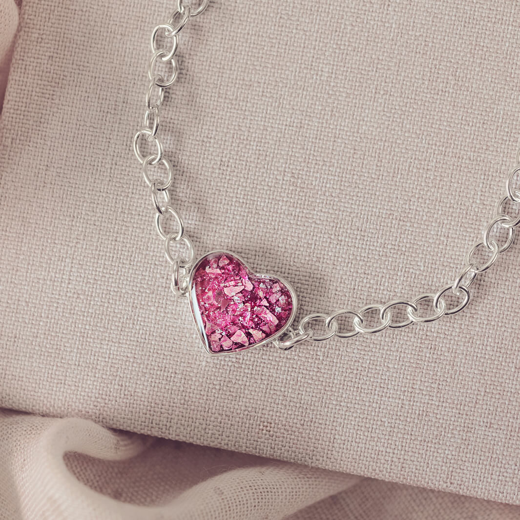 silver bracelet & heart charm, holding pink crystal, resin & cremation ashes. laying on a beige back ground 