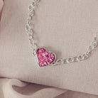 silver bracelet & heart charm, holding pink crystal, resin & cremation ashes. laying on a beige back ground 