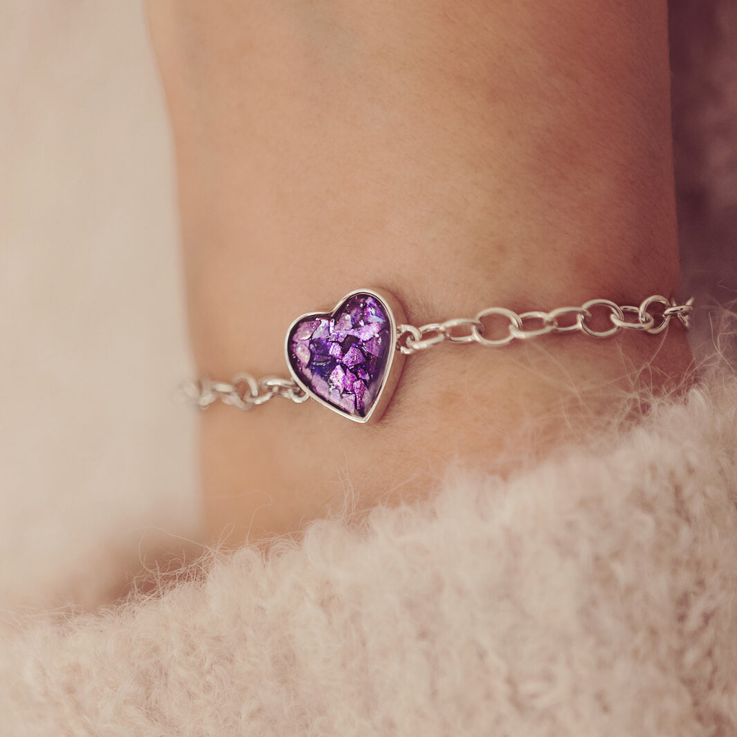 silver bracelet & heart charm, holding purple crystal, resin & cremation ashes. Worn on a ladies wrist.
