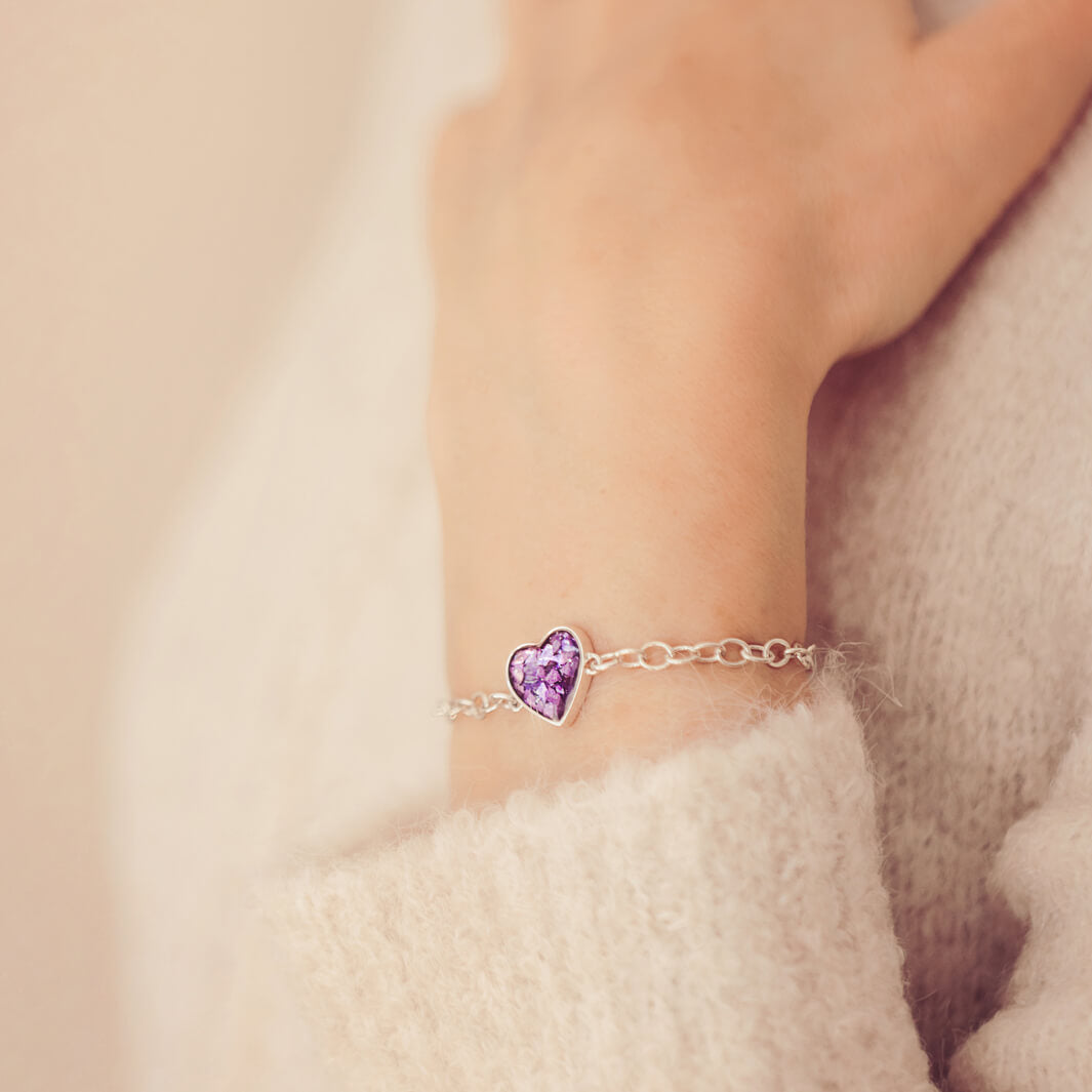 silver bracelet & heart charm, holding purple crystal, resin & cremation ashes. Worn on a ladies wrist.