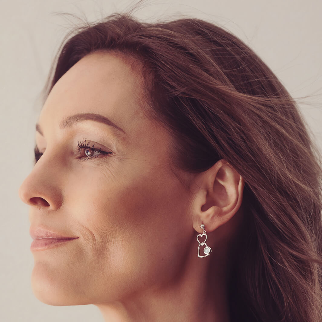 Silver Heart Dangle Earrings, holding cremation ashes, with clear crystals. Worn in a ladies ear.