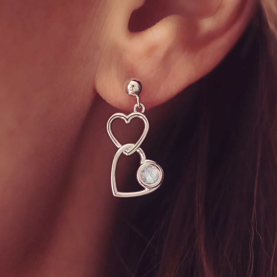 Silver Heart Dangle Earrings, holding cremation ashes, with clear crystals. Worn in a ladies ear.