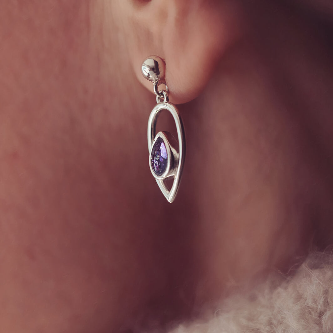 Cremation Ashes Peardrop Dangle Earrings filled with purple crystal and ashes, worn in a ladies ear