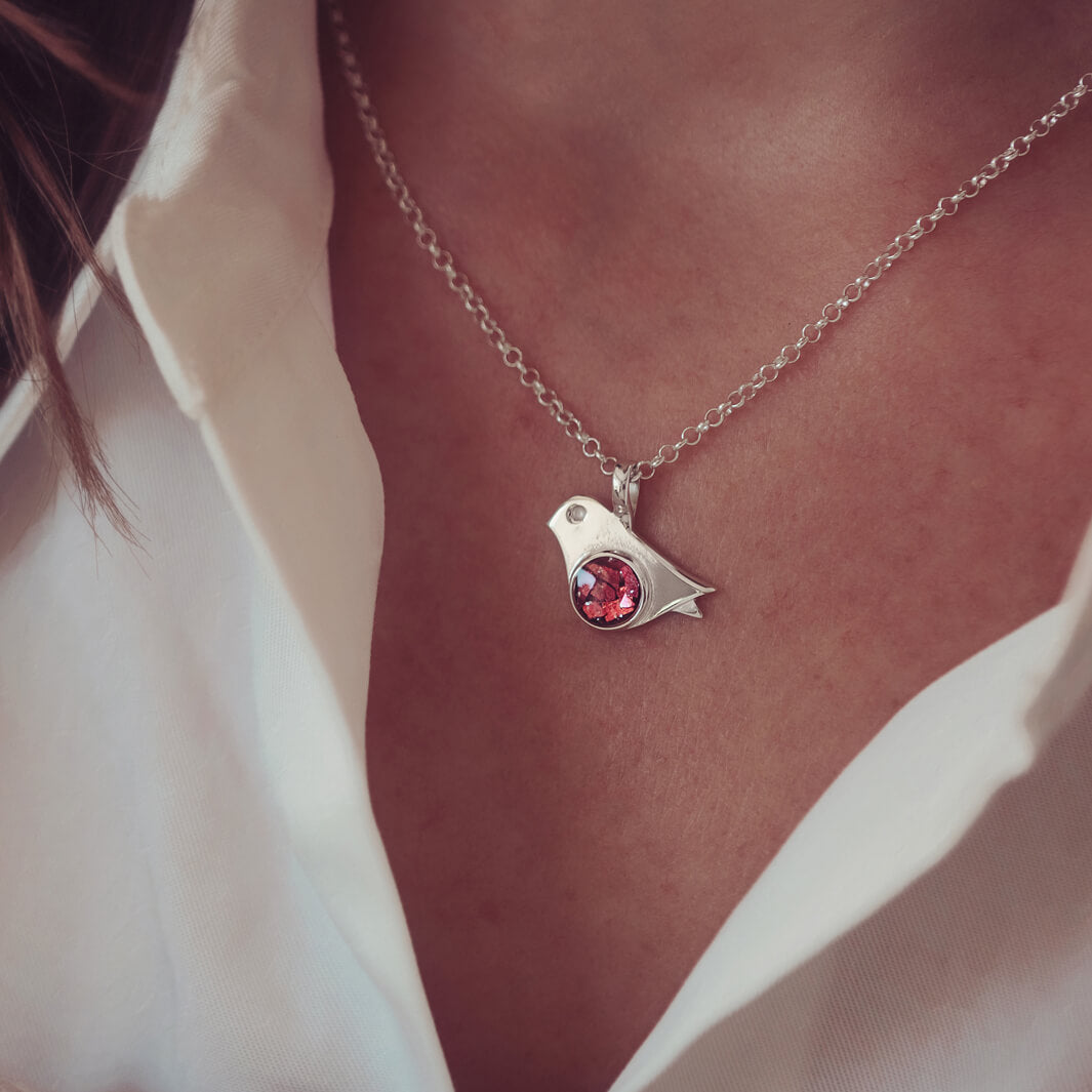 sterling silver robin necklace holding cremation ashes and red crystal, on a ladies neck