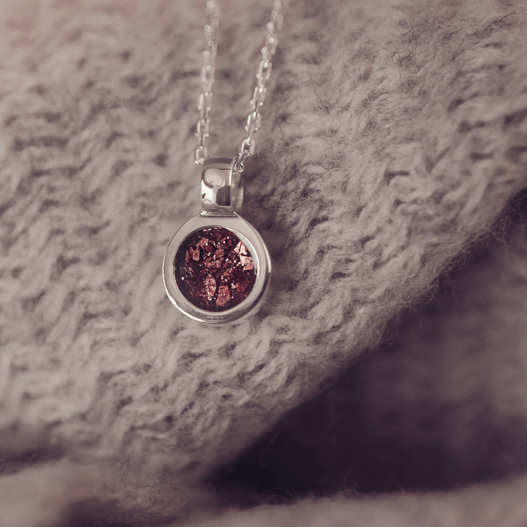 Silver necklace with a round pendant with brown gemstone, on a textured fabric background