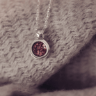 Silver necklace with a round pendant with brown gemstone, on a textured fabric background