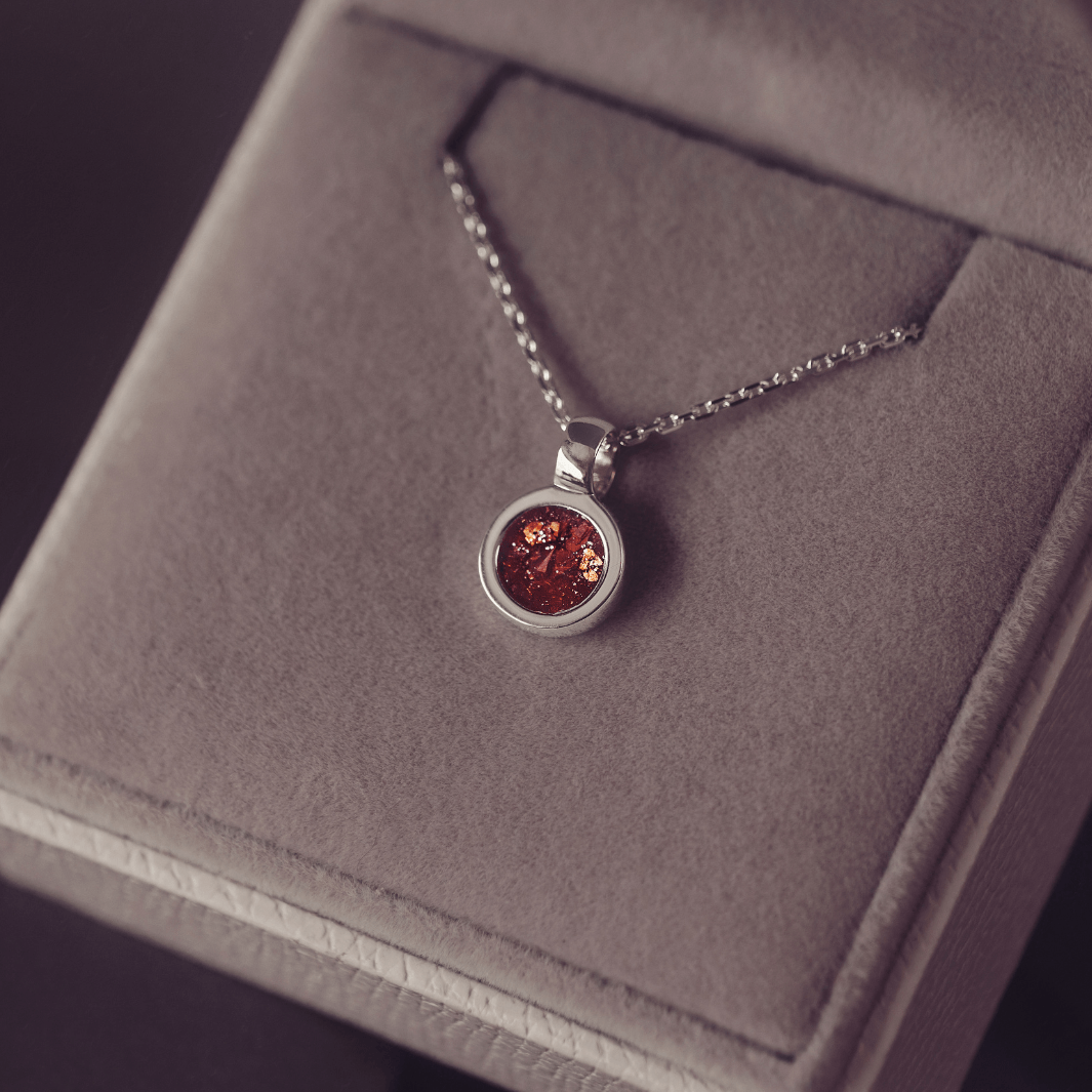 Silver necklace with a round pendant with orange gem, on a grey jewellery box