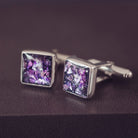 Square silver cufflinks containing cremation ashes, purple crystal and resin sat on a dark grey background 