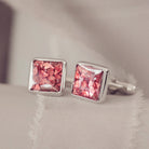 Square silver cufflinks containing cremation ashes, red crystal and resin sat on a beige fabric background 