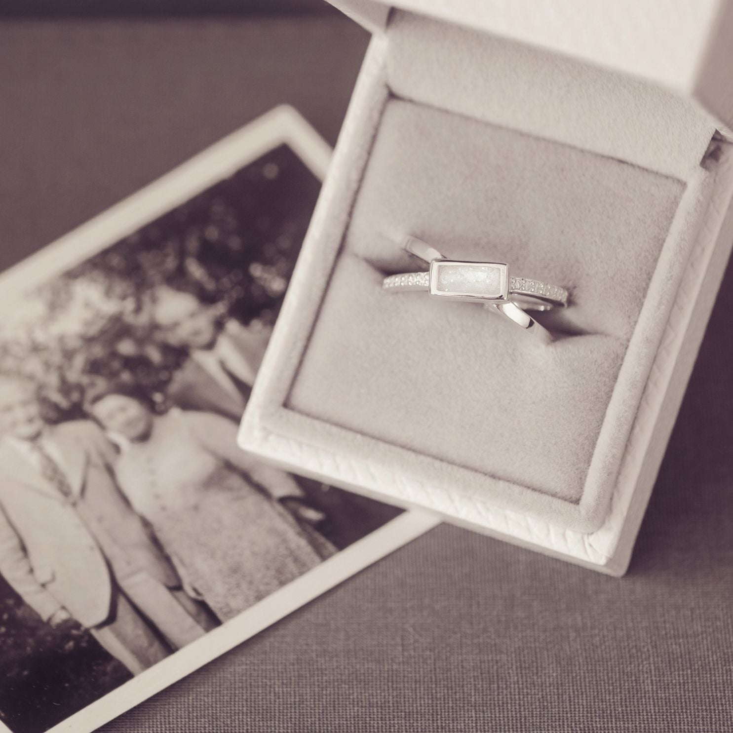 Silver ring in a box with an old photograph of two people in the background