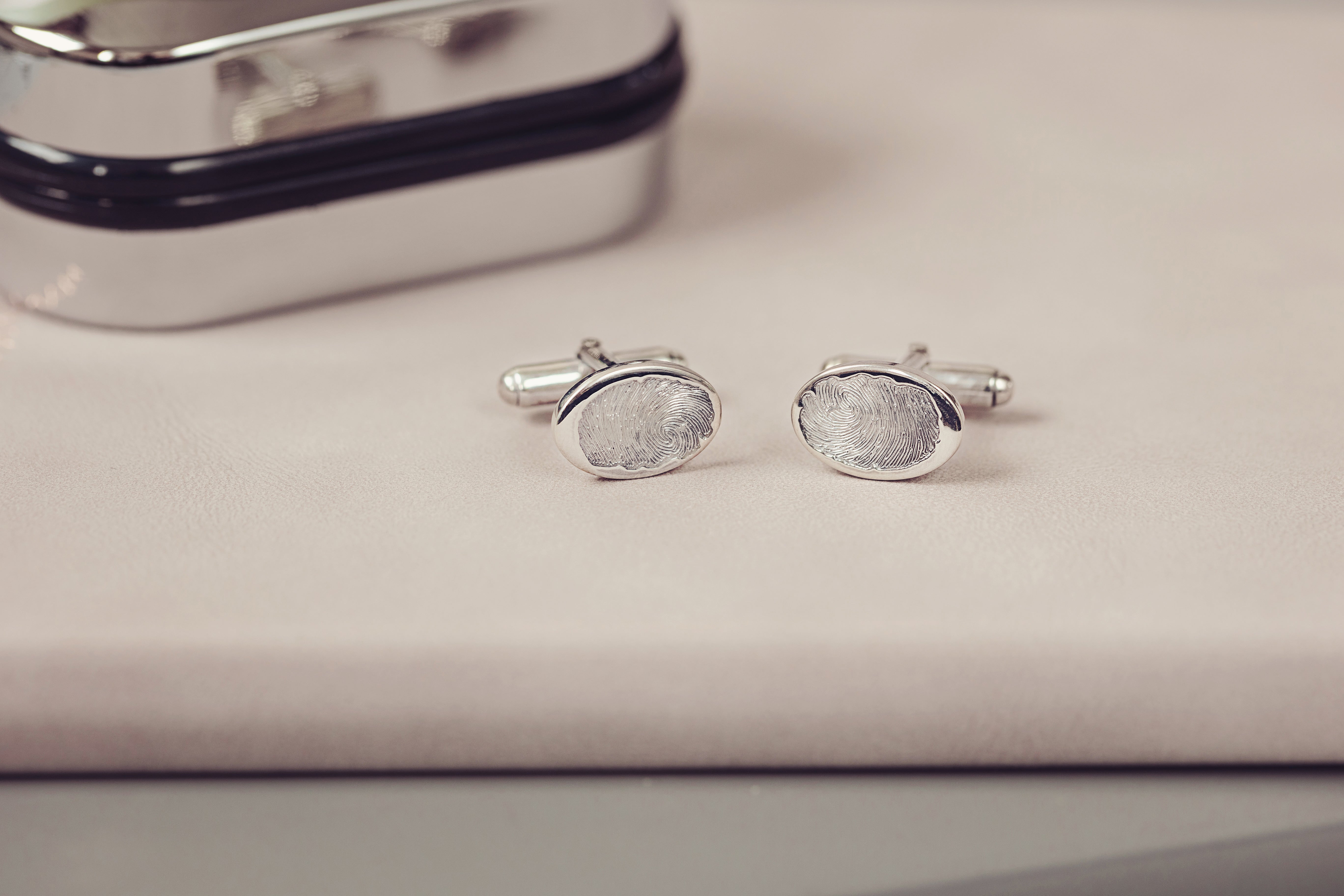 A pair of silver fingerprint cufflinks with a silver cufflink case displayed next to them