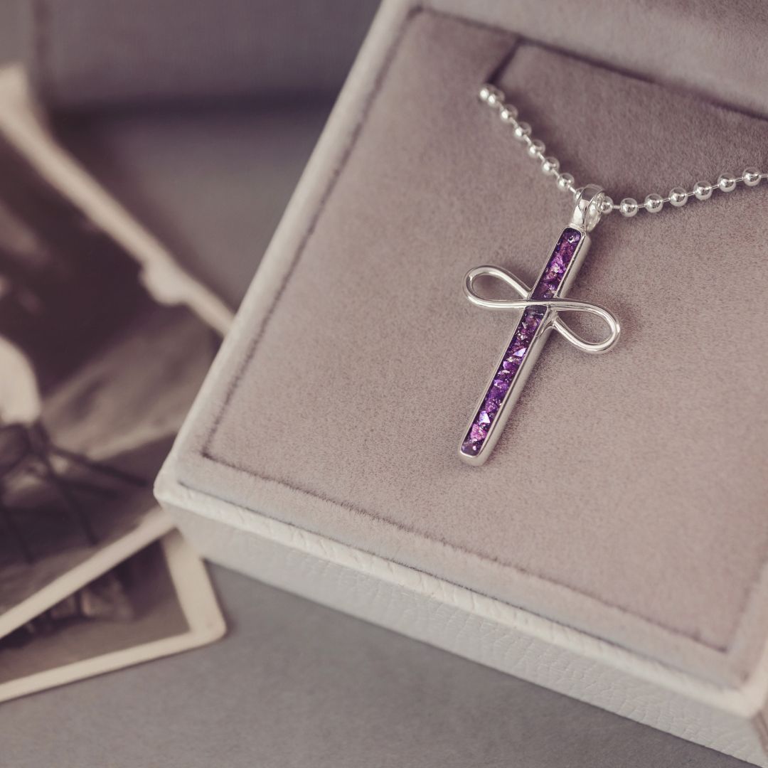 Silver cross necklace with purple stones on a display box