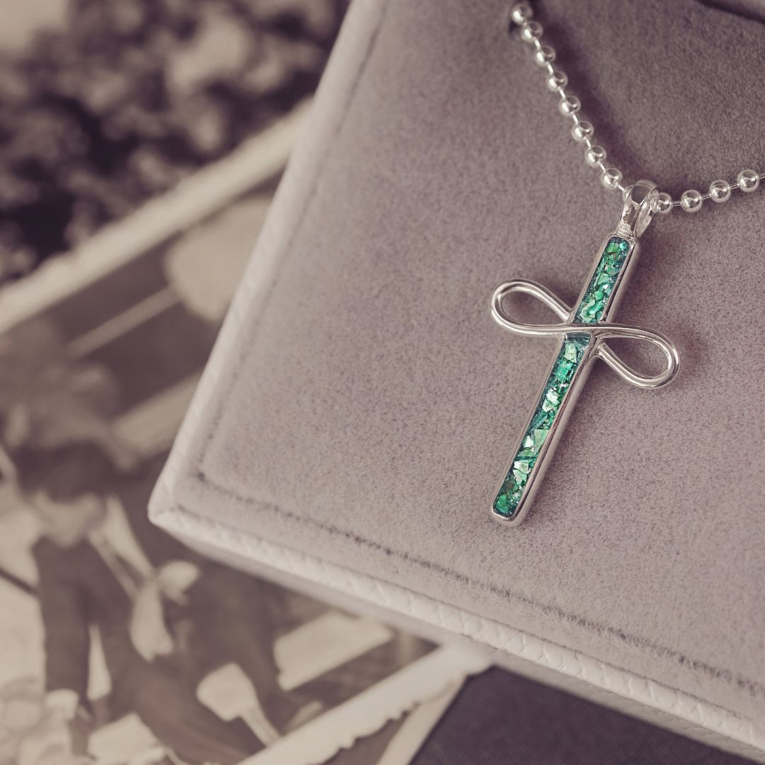 Necklace with a cross pendant featuring green stones on a gray surface.