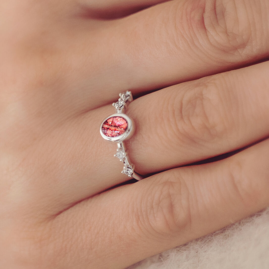 silver ring band with oval stone, created from cremation ashes & red crystal. Worn on a ladies hand.