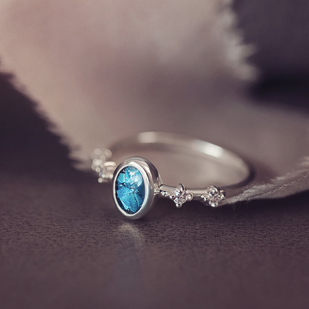 silver ring band with oval stone, created from cremation ashes & blue crystal. Sat on a dark grey background