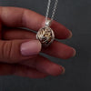 Demo video of womans hands with pink nails showing how to fill a silver leaf cage urn necklace pendant. the pendant has a gold ball inside the cage, to fill with ashes. the video shows her using a wooden stick to fill the ball with cremation ashes.