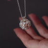 A demonstration video of an silver ashes urn necklace with a tree patterned design and a rose gold ball inside. The video shoes a woman's hands taking the necklace apart and filing it with ashes.