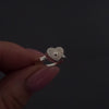 womans hands with pink nails demonstrating how to fill a silver heart ring agaisnt a dark background. It shows her unscrewing the screw and using a funnel to fill the ring with ashes. its then displayed in a grey jewellery box at the end.