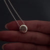 womans hands with pink nails demonstrating how to fill a silver round pendant agaisnt a dark background. It shows her unscrewing the screw and using a funnel to fill the pendant with ashes. its then displayed in a grey jewellery box at the end.
