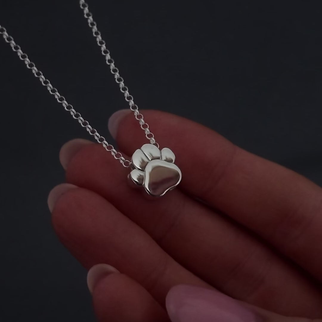 womans hands with pink nails demonstrating how to fill a silver paw ashes necklace. The necklace has "willow" engraved on the back. It shows her unscrewing the chamber and adding the ashes with a funnel. Its then displayed in a jewellery box.