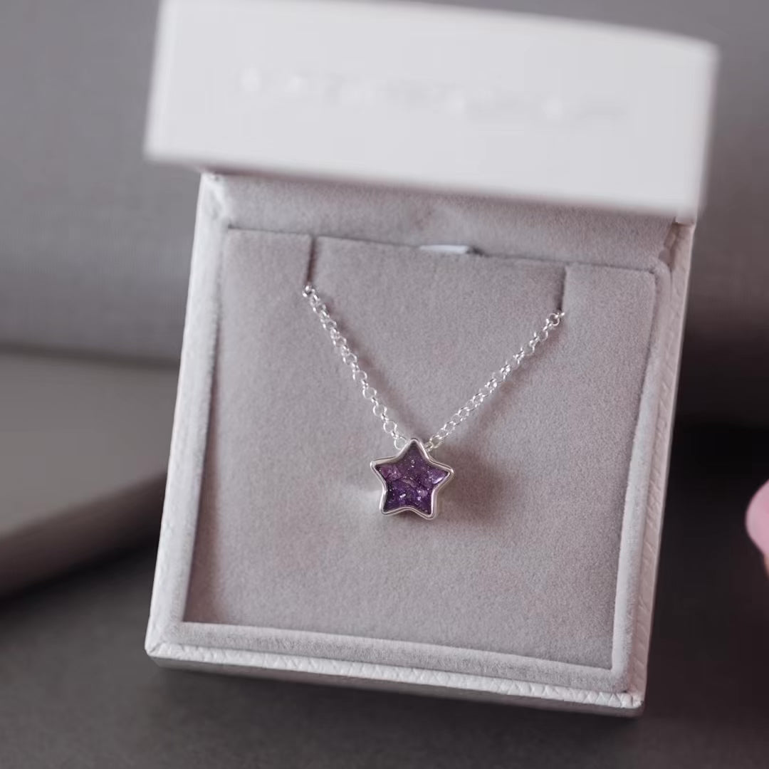 Silver ashes star necklace with purple crystals in a grey jewellery box held by a women's hand