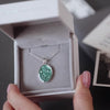 Silver oval ashes pendant necklace with green crystals in a grey jewellery box held in a women's hand
