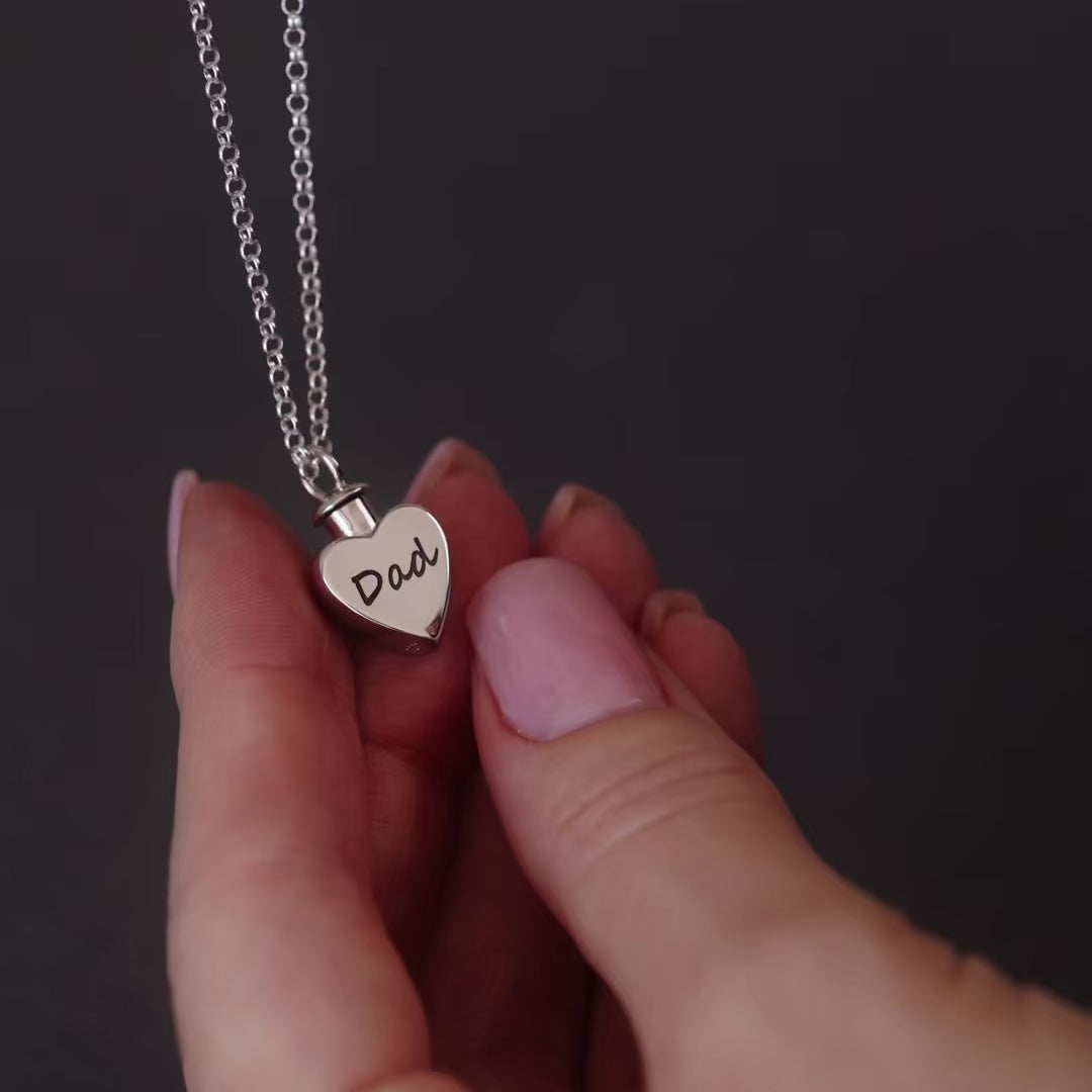 demo video of a silver heart ashes locket necklace thats says "Dad" on it. the video shows a woman's hand unscrewing the necklace then filling it with ashes 
