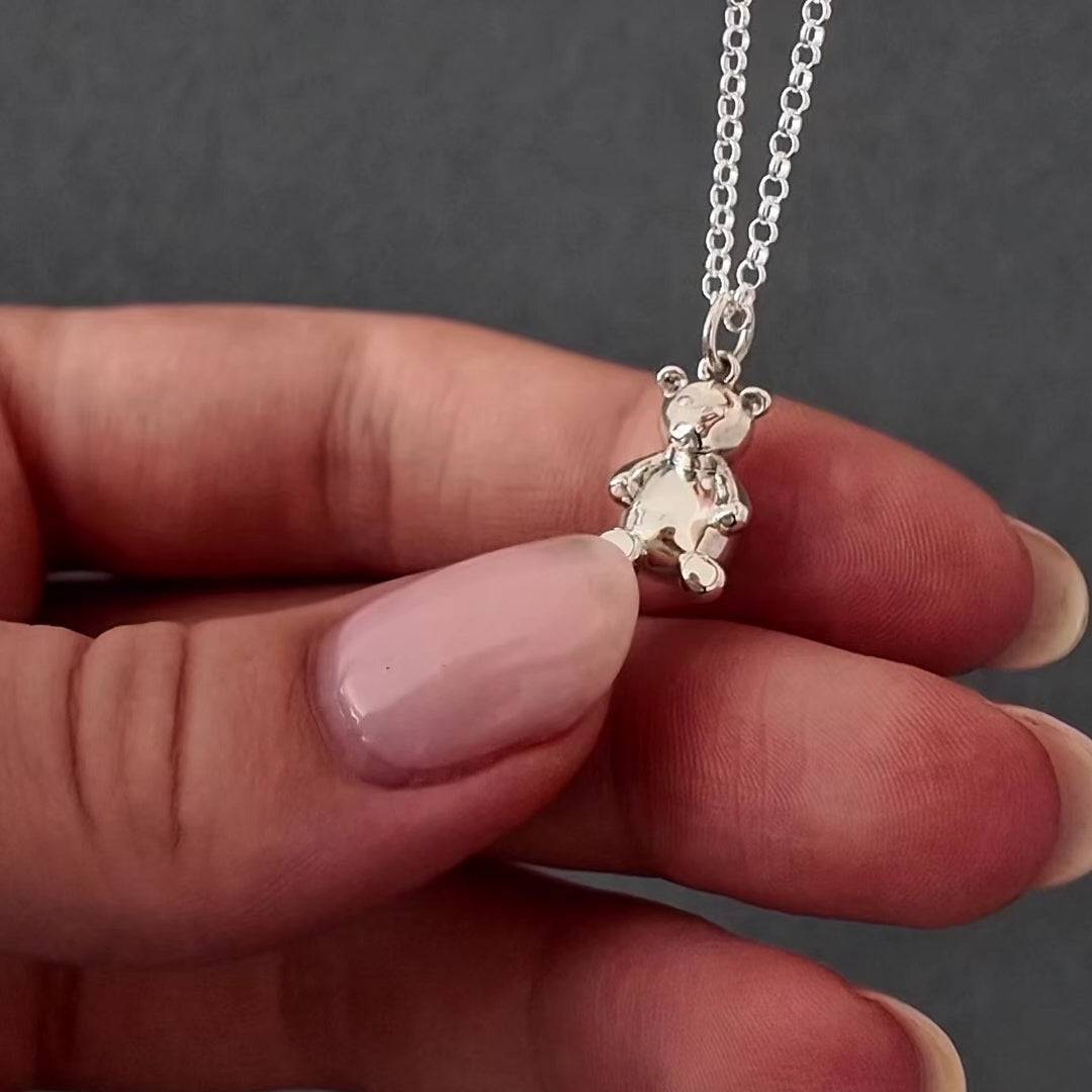 Demo video of womans hands with pink nails showing how to fill a silver teddy bear urn necklace pendant. it shows her unscrewing the bottom of the pendant with a screwdriver and using a funnel to fill the pendant with cremation ashes. the screw is then screwed back on and the necklace is displayed in a grey jewellery box. 