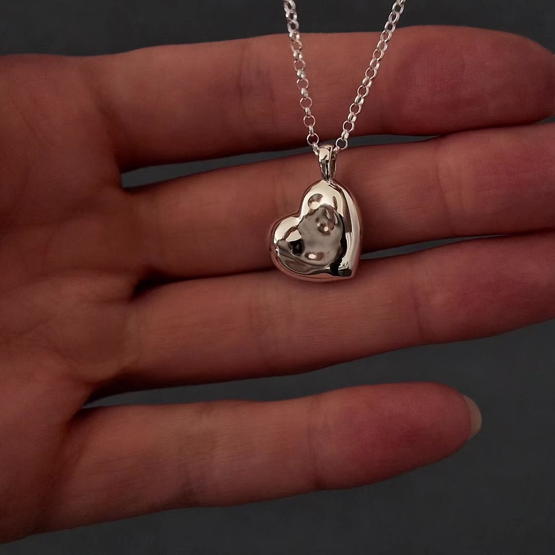 Demo video of womans hands with pink nails showing how to fill a silver scluplted heart necklace pendant. the pendant has "miss you" engraved on the back. the video shows her unscrewing the back on the pendant then using a funnel to fill the heart with cremation ashes.