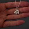 Demo video of womans hands with pink nails showing how to fill a silver scluplted heart necklace pendant. the pendant has "miss you" engraved on the back. the video shows her unscrewing the back on the pendant then using a funnel to fill the heart with cremation ashes.
