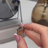 demonstration video showing a woman's hands filling an ashes urn necklace. the urn necklace is a teardrop shaped silver pendant with "lots of love Dad xxx" written on the front in true handwriting. the video shows the woman's hands unscrewing the pendant then filling it with ashes. the woman has pink nails with white tips. there is a black mirror, brown flower vase and a grey trinket dish in the background.